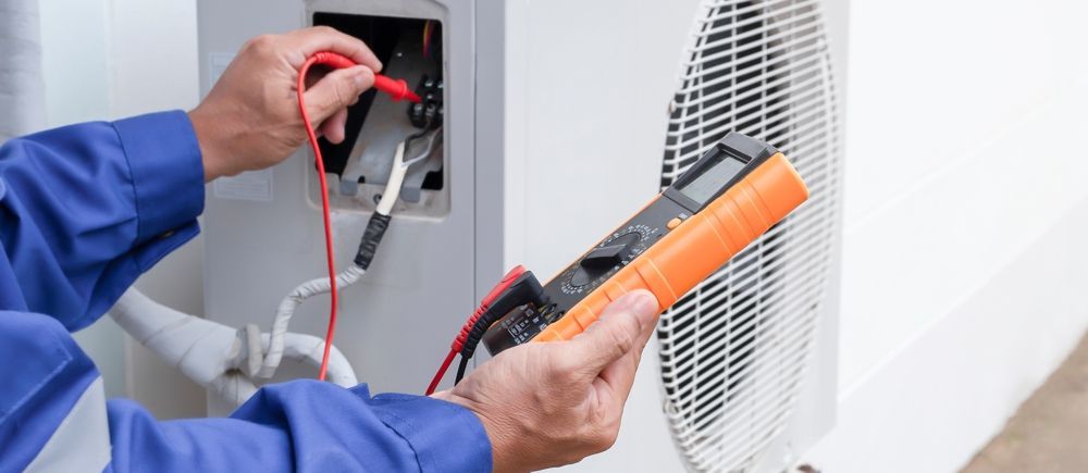 Electrician using a multimeter to test an air conditioning unit's electrical components.