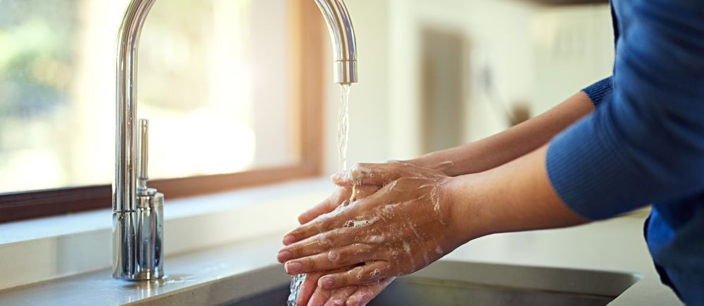Person washing hands under a running faucet.