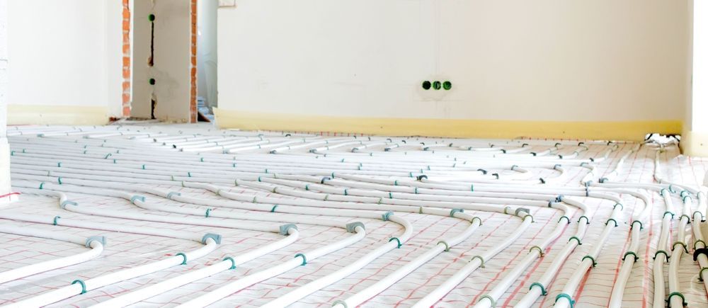 Floor with radiant heating system installed, white pipes, green connections, near white walls.