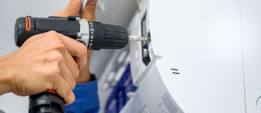 Person using a power drill to install or repair a white appliance.