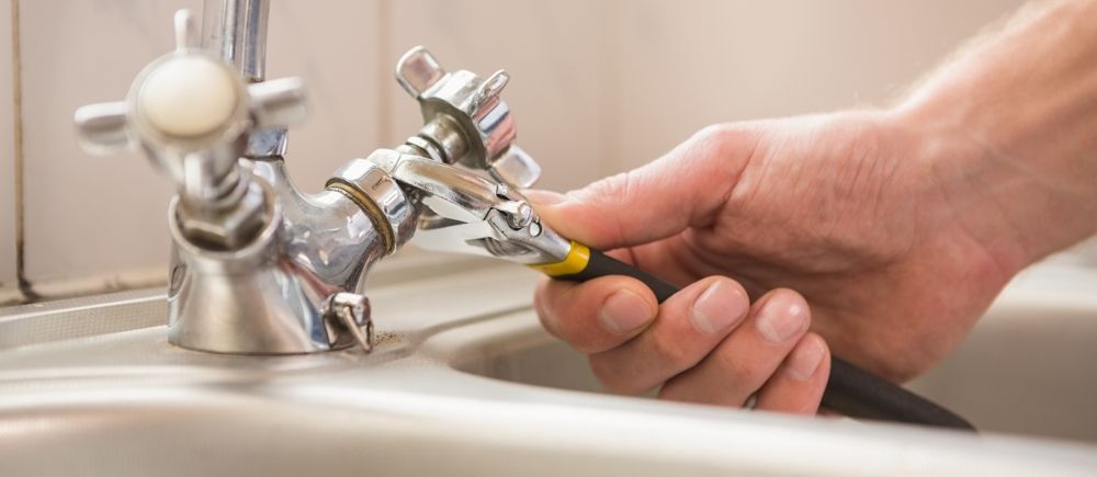 A person's hand is fixing a faucet with a wrench in a sink.