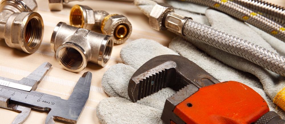 Plumbing tools, including an adjustable wrench and fittings, arranged on a surface.
