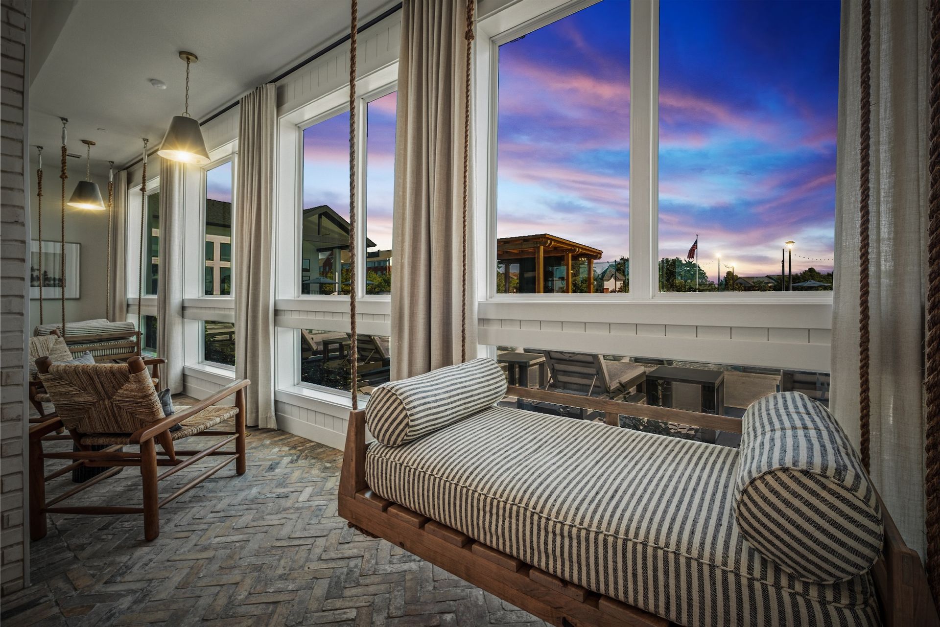 Sunroom with swing bed, exposed beams, brick floor, large windows with sunset view.