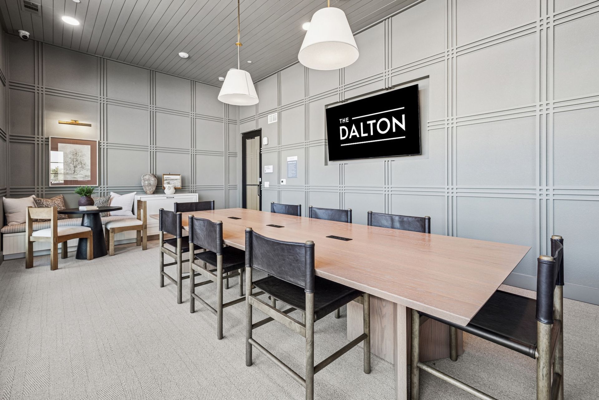 Conference room with long table, black chairs, TV screen. Gray panel walls, light fixtures, and carpet.