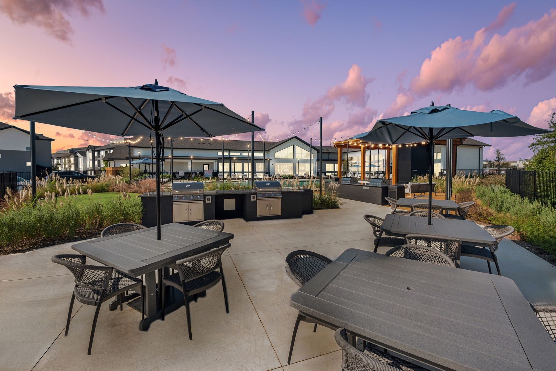 Outdoor patio with tables, chairs, umbrellas, and grills under a sunset sky.