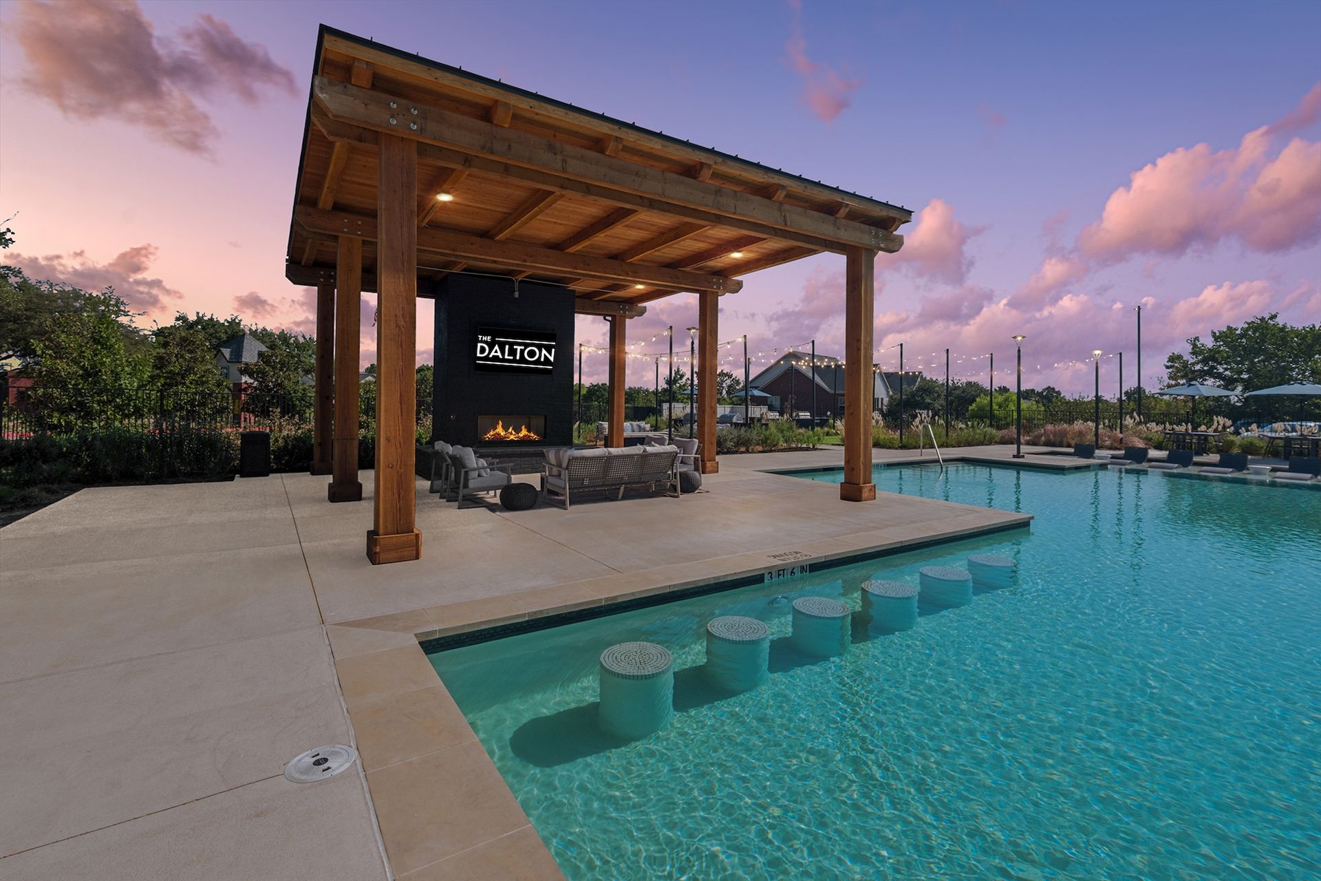 Poolside pavilion with fireplace; wooden beams, water, and sunset sky.