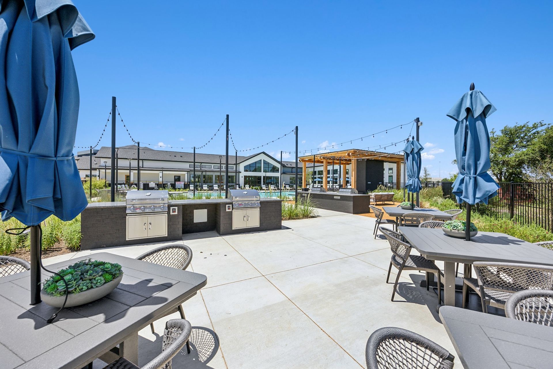 A patio with tables and chairs and umbrellas and a grill.