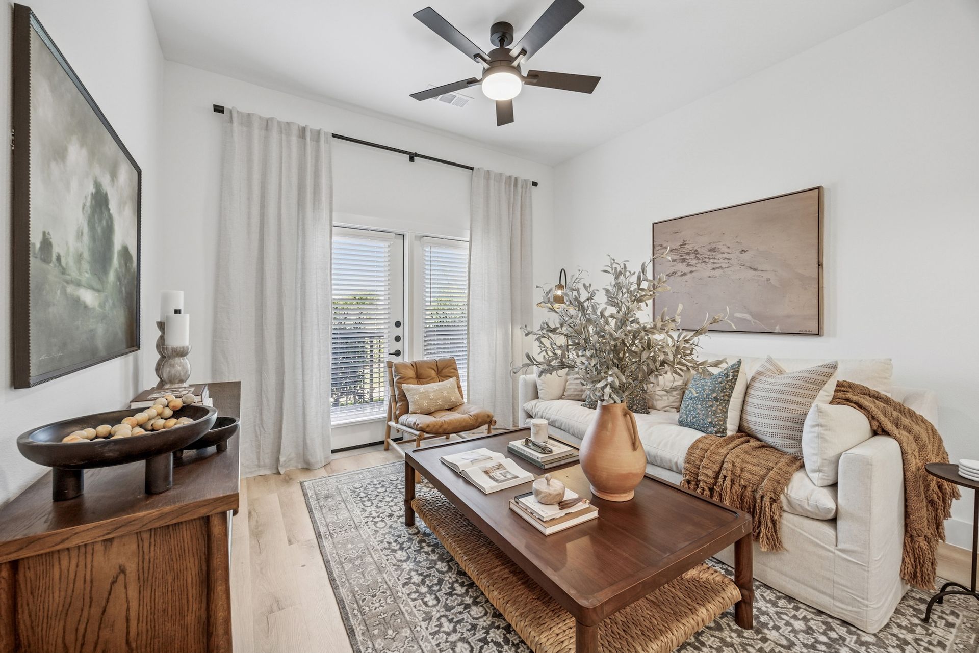 A living room with a couch , chair , coffee table and ceiling fan.