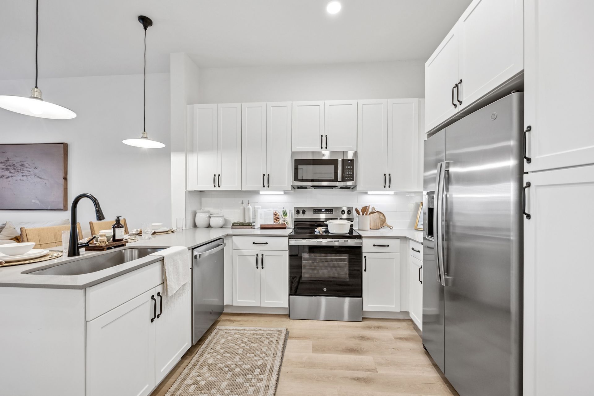 Modern white kitchen with stainless steel appliances, light wood floors, and overhead pendant lights.
