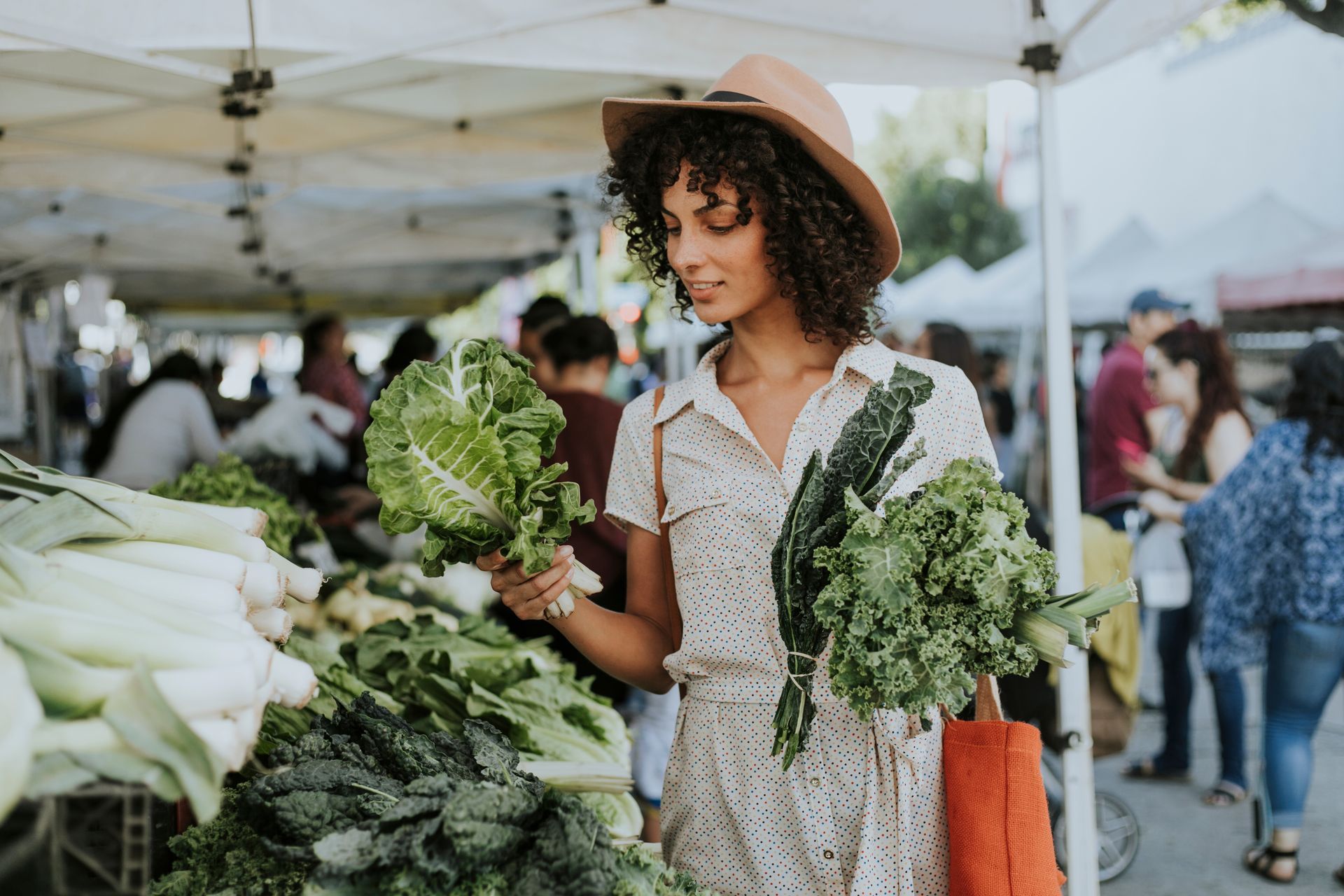 A woman is holding a bunch of lettuce at a farmers market.