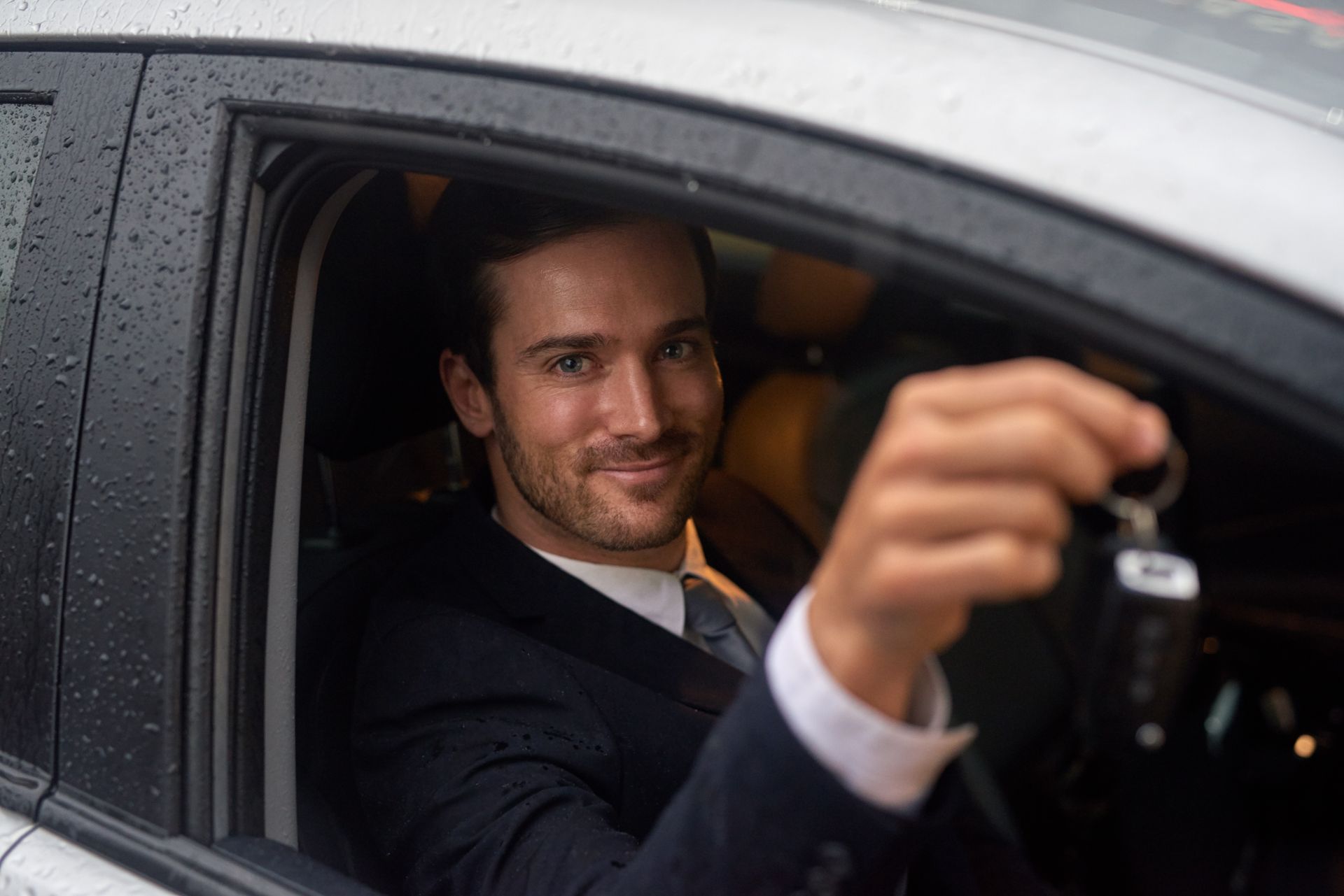 A man in a suit is sitting in a car holding a car key