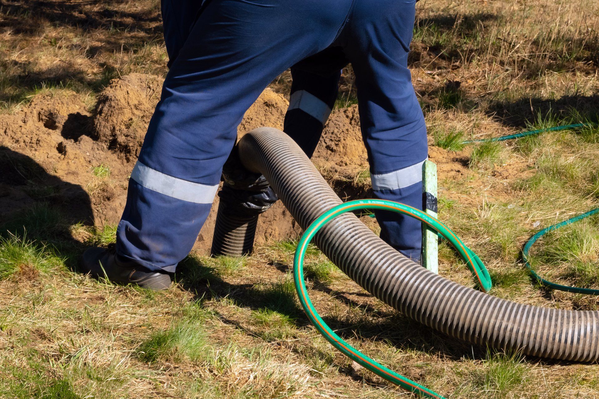 Man worker using sewage pumping machine to unclog blocked manhole during outdoor sewer cleaning service.