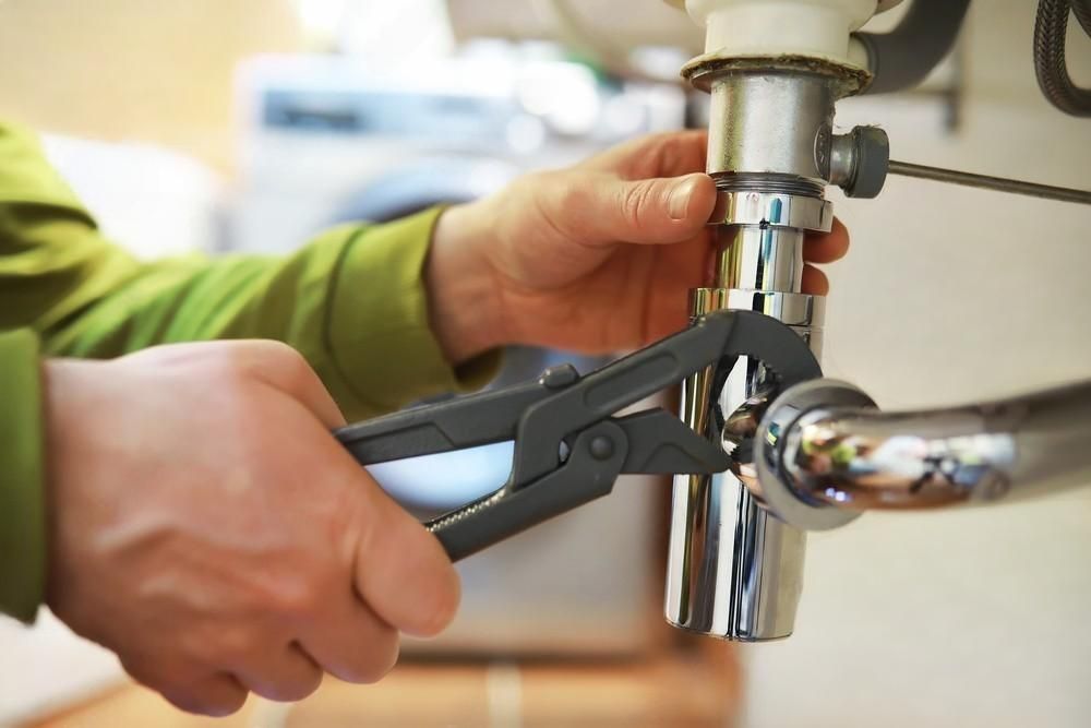 A person is fixing a sink pipe with a wrench.