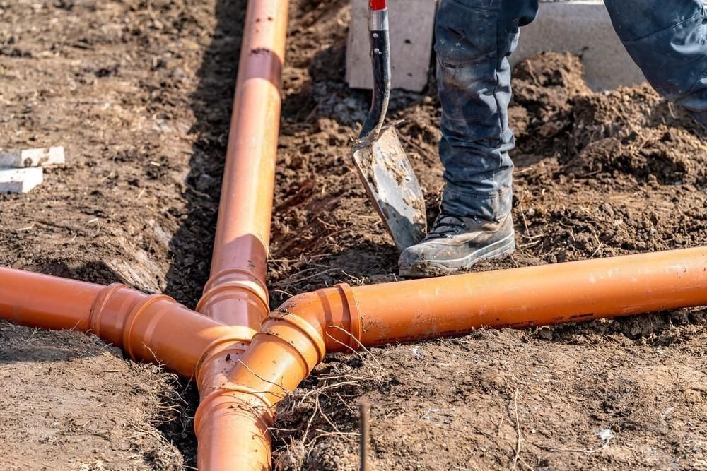 A man is digging a hole in the ground to install drain pipes.