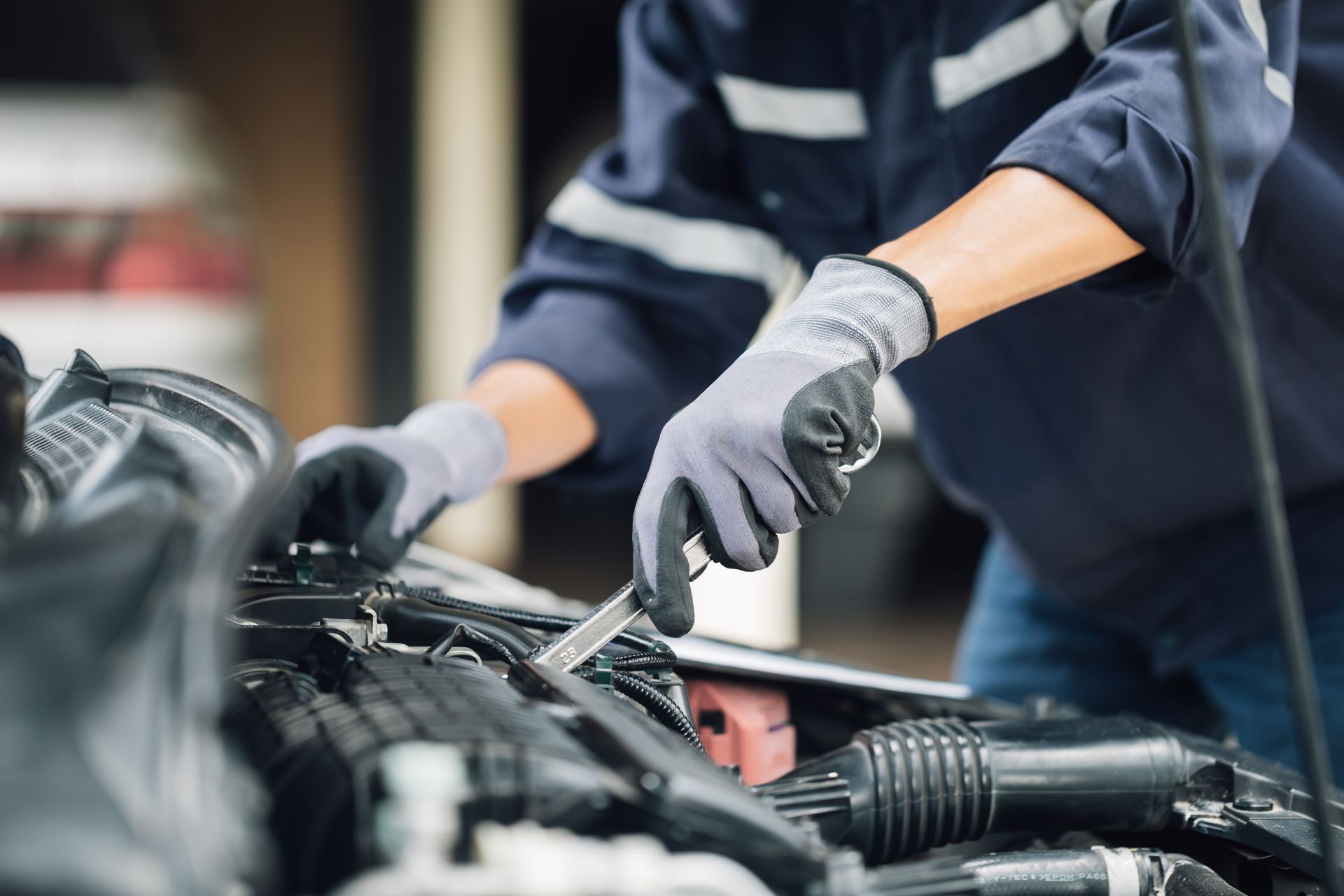 A technician is performing car maintenance under an open hood.
