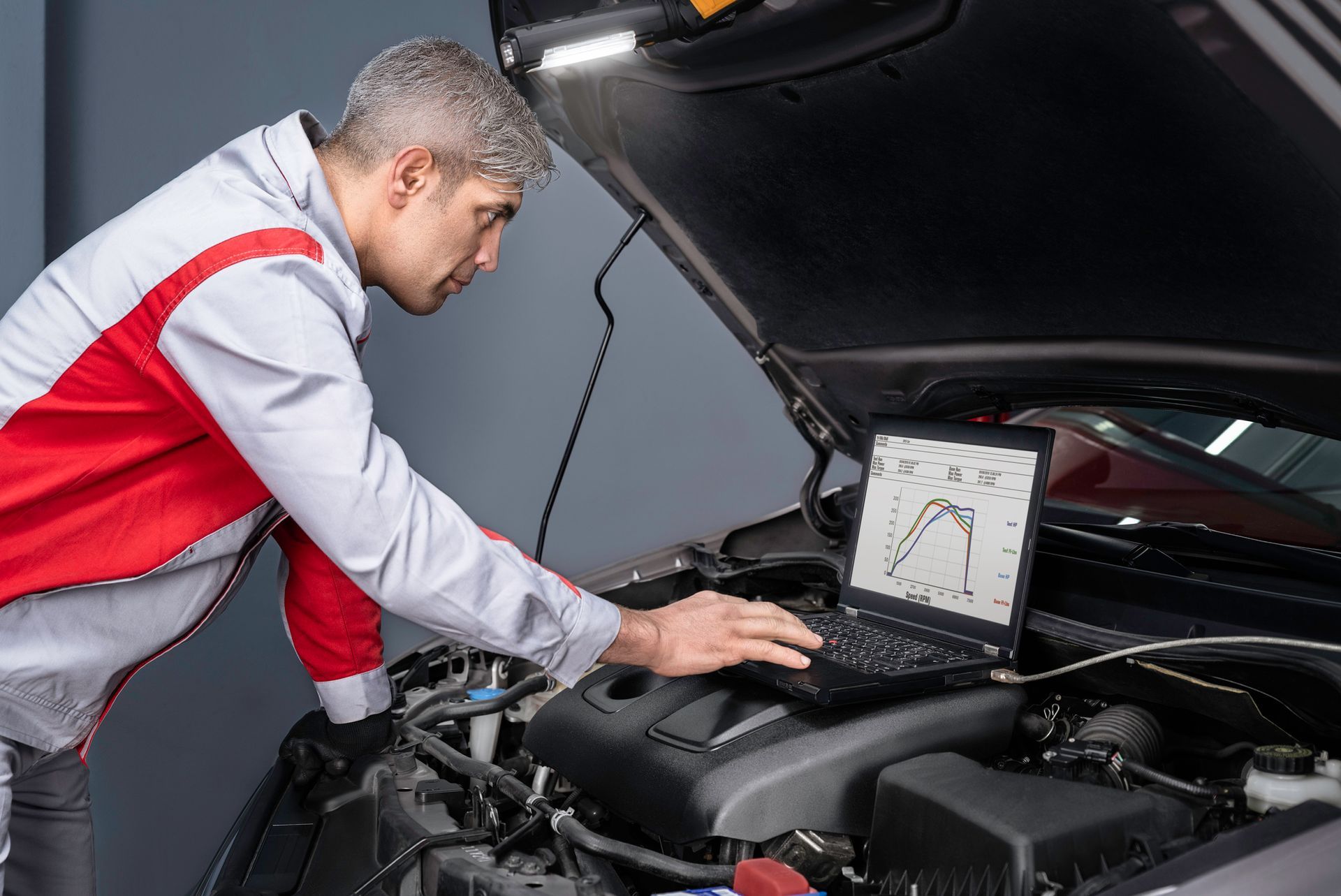 An Audi auto mechanic searching the engine for problems with a laptop.
