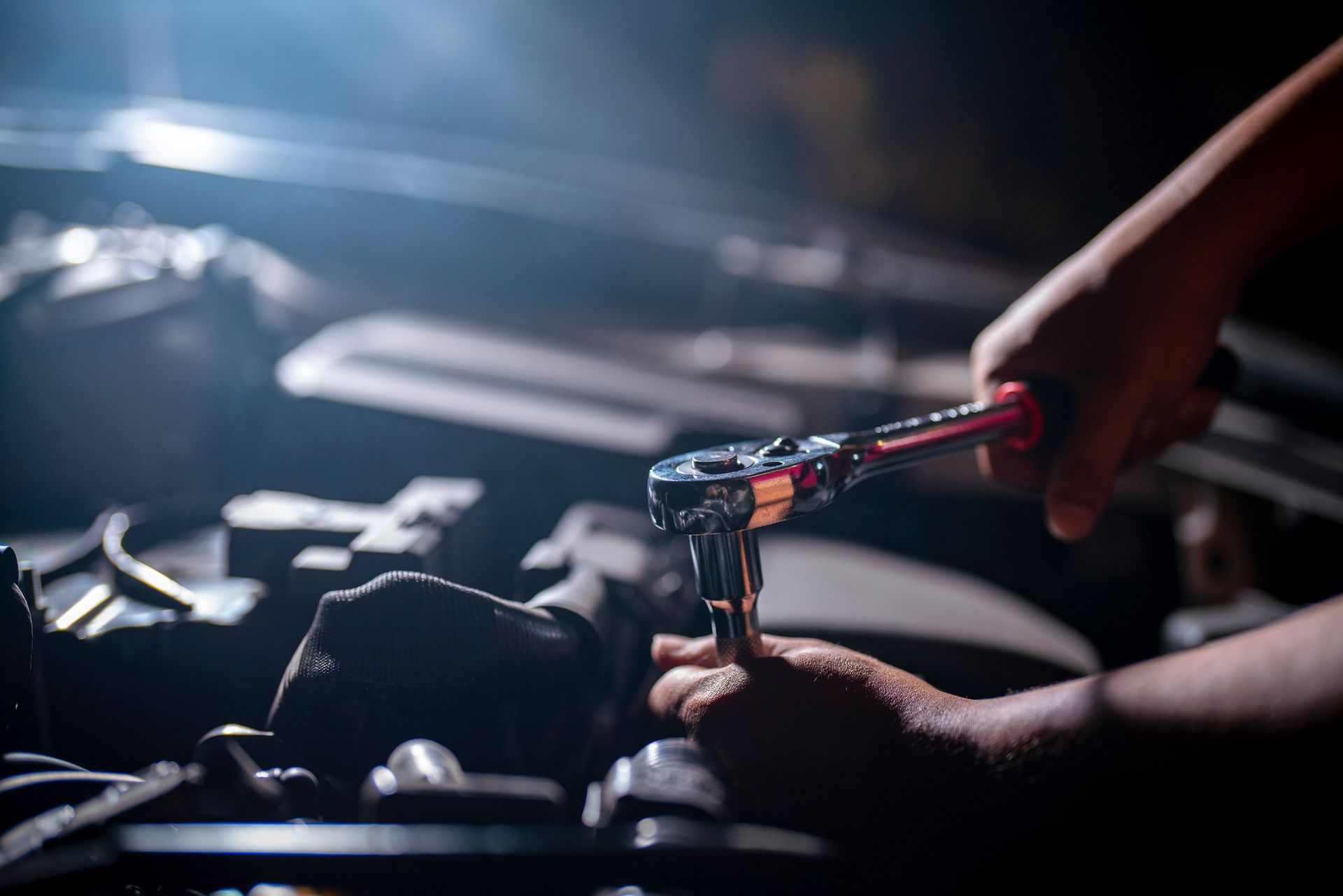 Close-up of a hand using a ratchet wrench to tighten a bolt under a car hood.