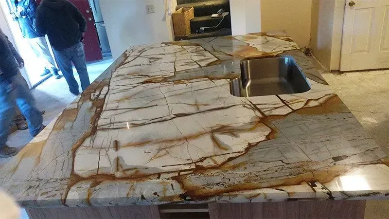 Marble countertop with a sink, featuring brown and white veining, with men in the background.