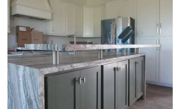 Kitchen island with gray-green cabinets, light granite countertop, and stainless steel supports for an overhang.