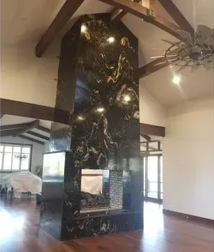 Black granite fireplace with gold veining, in a room with wooden beams, and hardwood floors.