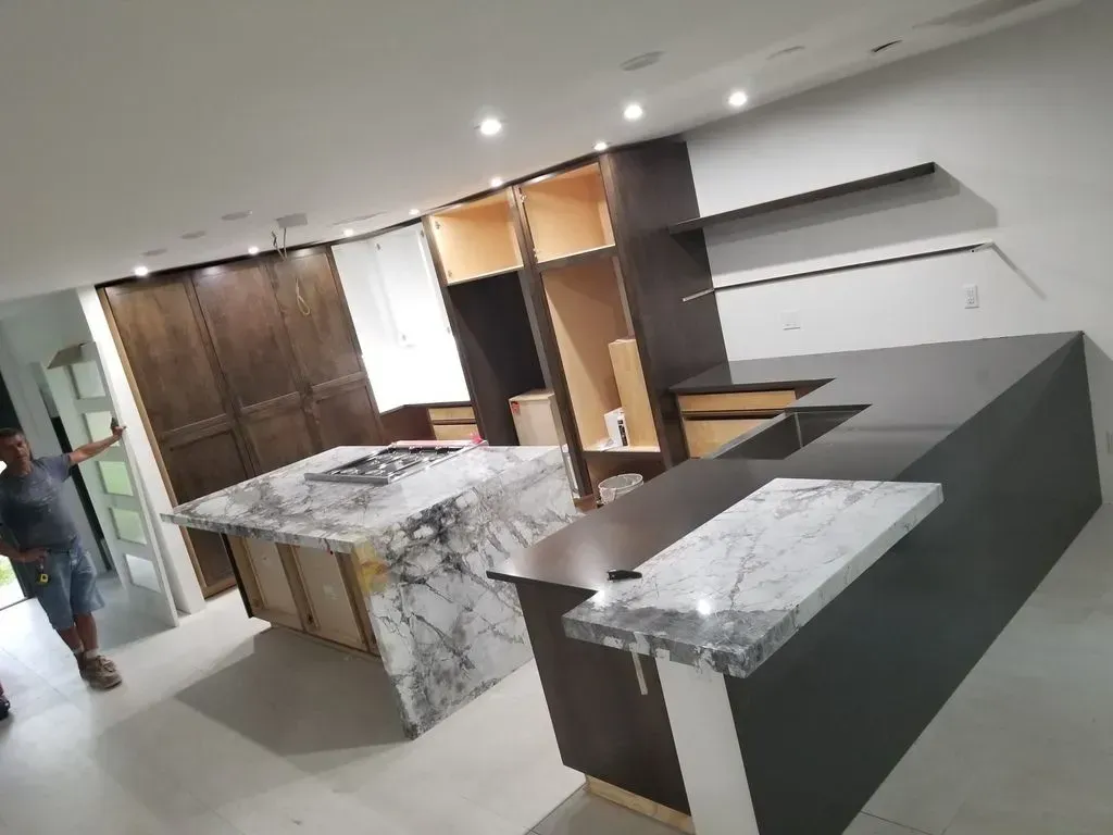 Modern kitchen under construction with two islands, cabinets, and a person.