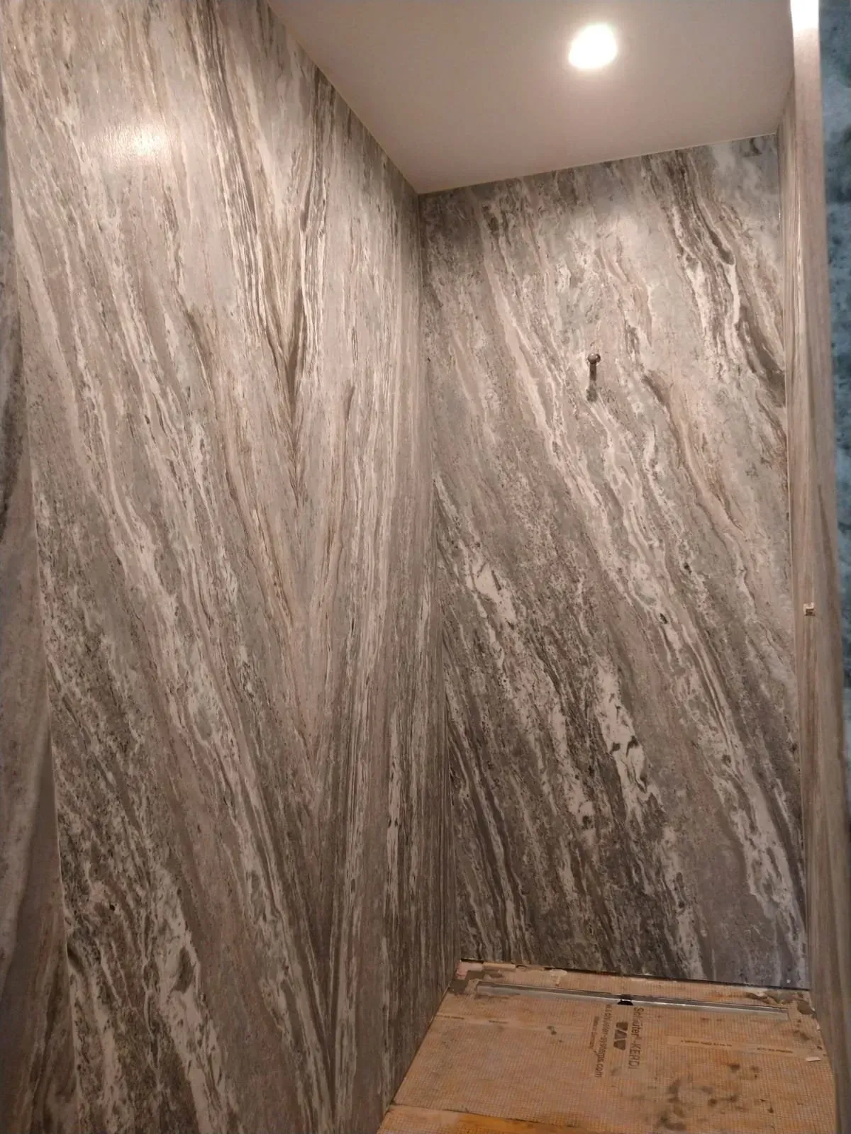 Gray and white veined stone wall in a corner of a room, with a recessed ceiling light.