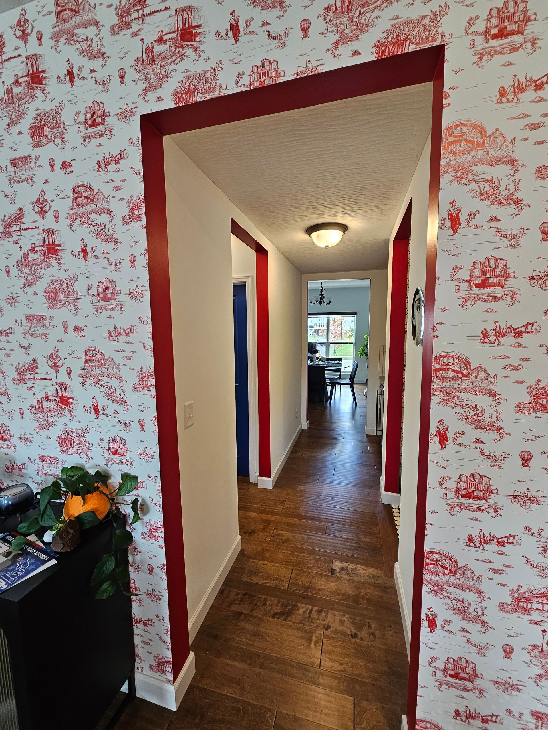 Hallway with red trim, red and white floral wallpaper, and wooden floors.