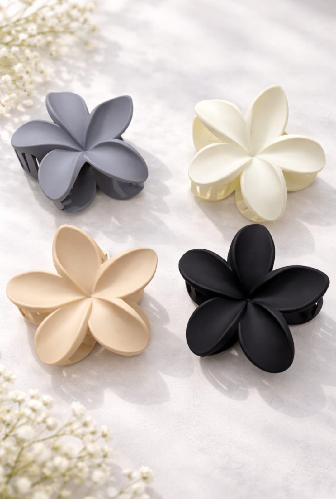 Cuatro horquillas para el cabello con forma de flor en color gris, blanco, beige y negro
