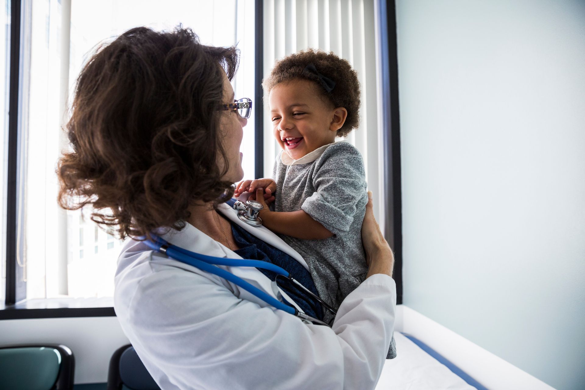 Doctor holding and smiling at a laughing child; clinic room.