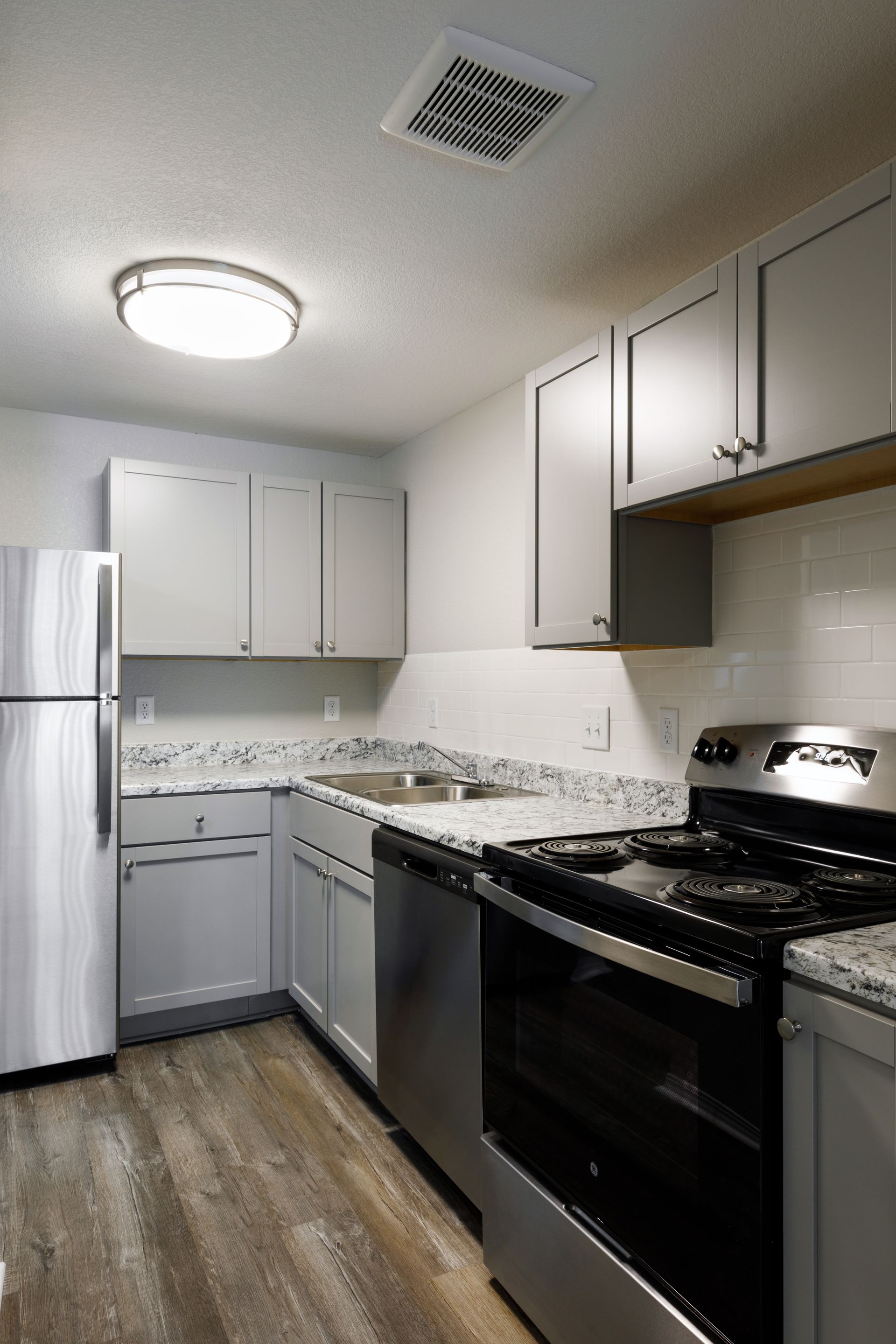 Gray kitchen with stainless steel appliances, light cabinets, granite countertops, and wood-look flooring.