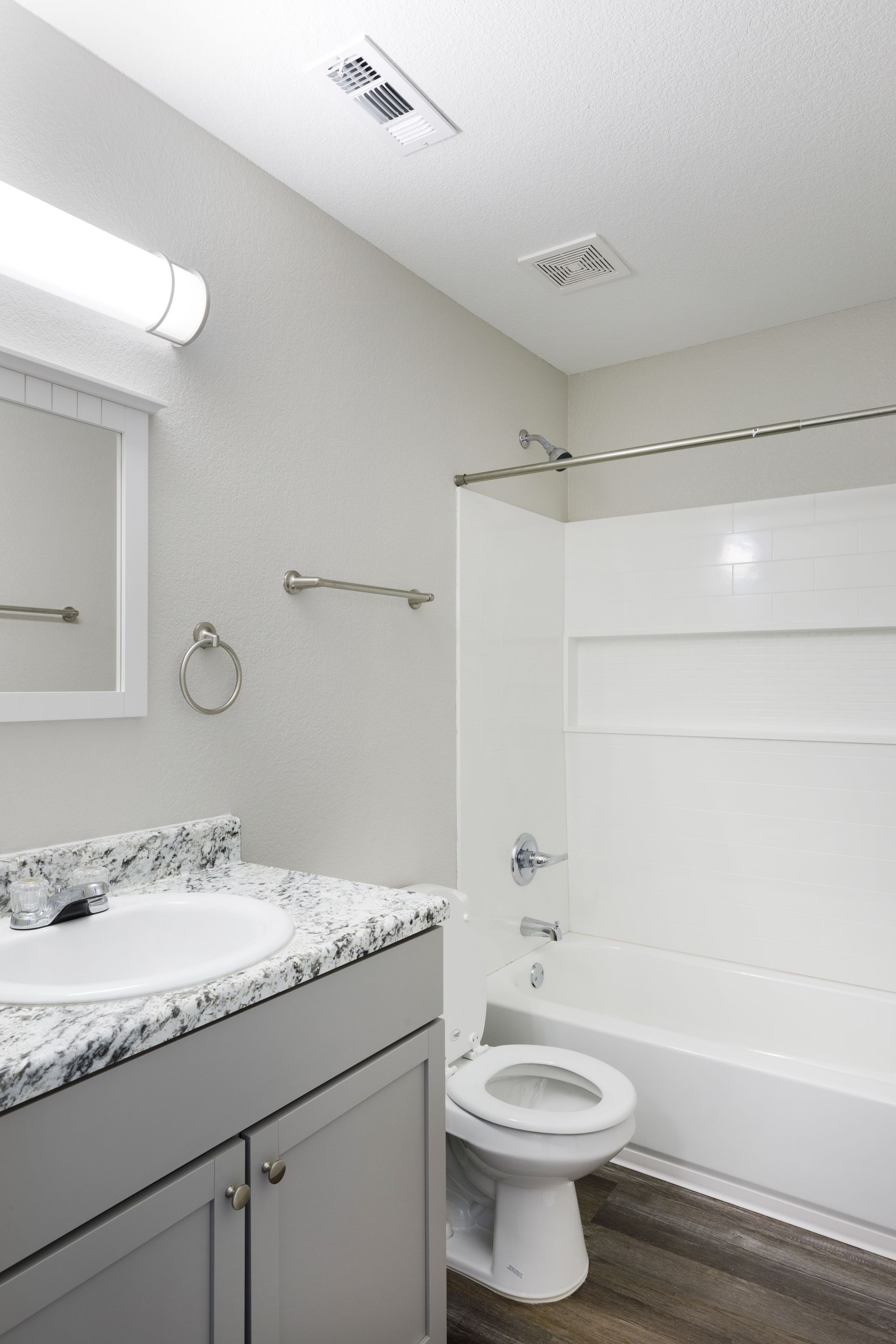 Bathroom with white tub, vanity, and toilet; gray walls, wood-look floor.