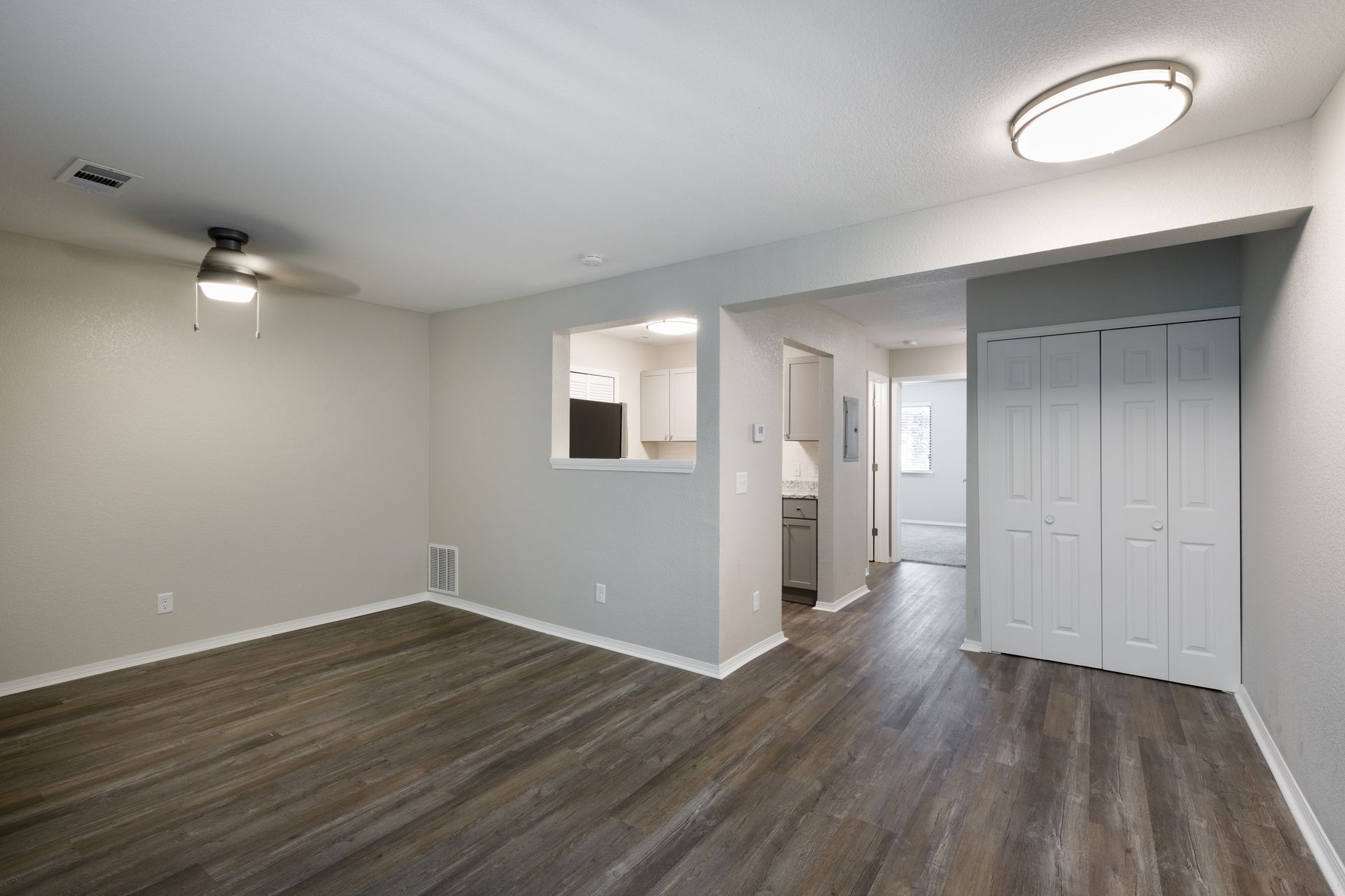 Empty living room with gray floors, white walls, and an entryway to the kitchen and a closet.