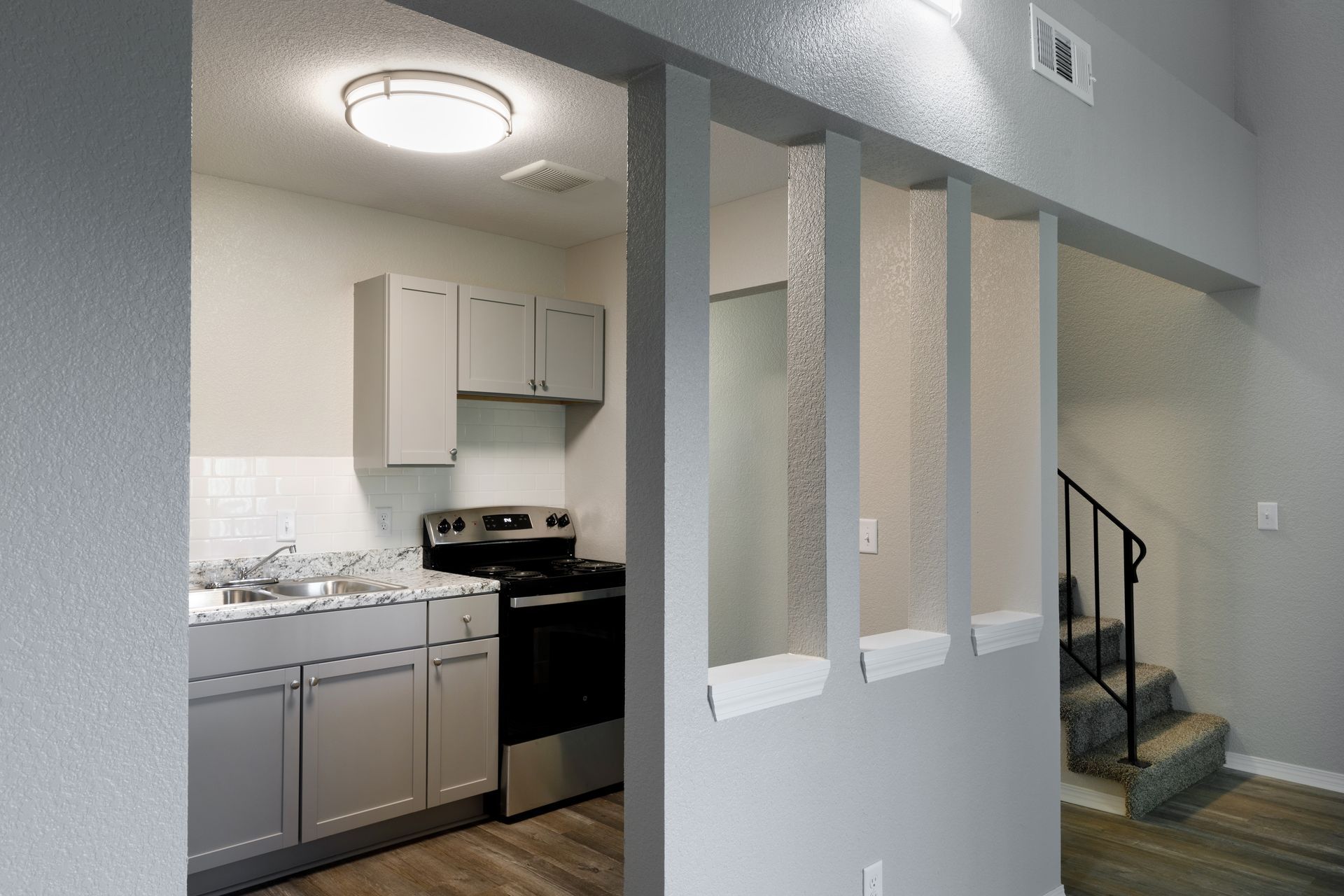 Kitchen with gray cabinets, stainless steel appliances, and a partial wall with stairs visible.