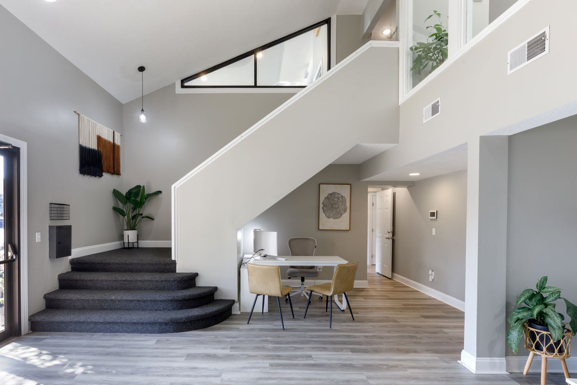 A bright, open interior with a staircase, dining area, and large windows, gray walls, and wood flooring.
