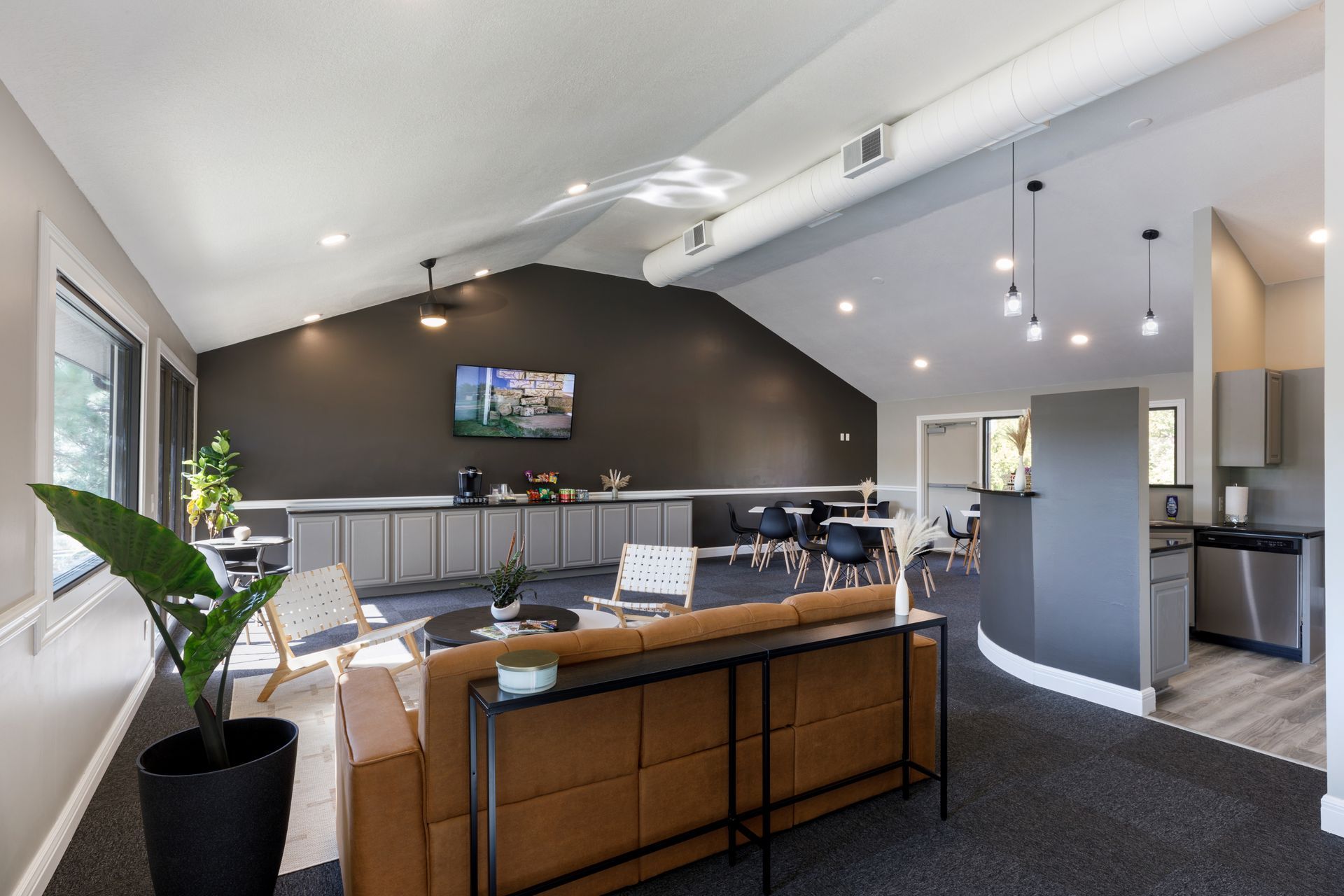 Modern lounge area with dark gray accent wall, leather couch, seating, and small kitchen.