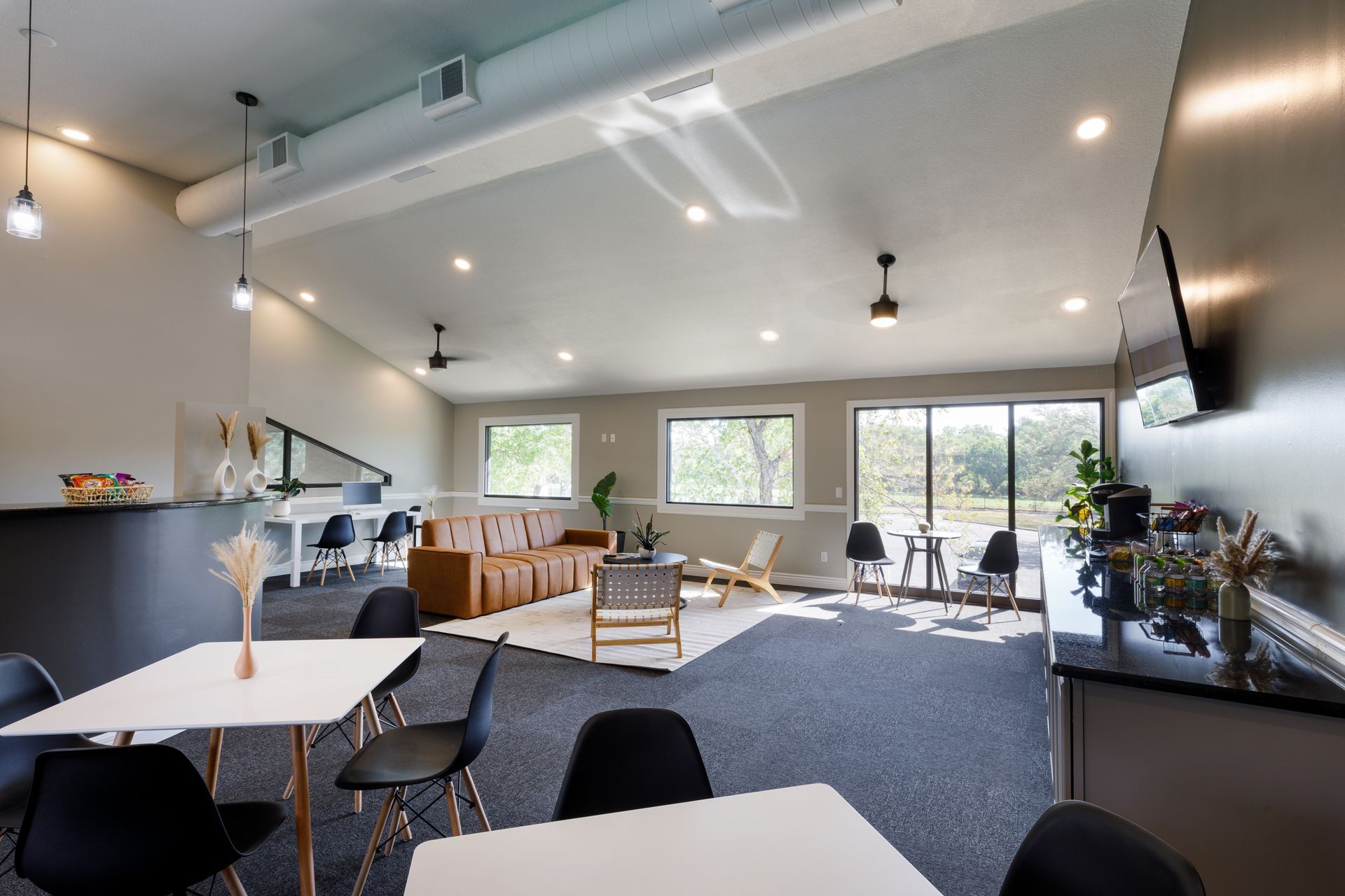 Modern lounge with seating, large windows, coffee station, and minimalist decor.