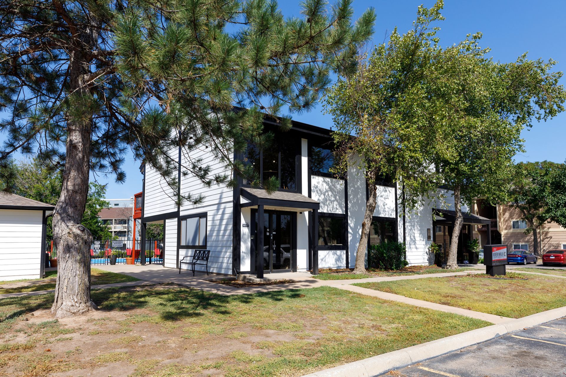 Two-story white apartment building with black trim and trees in front.