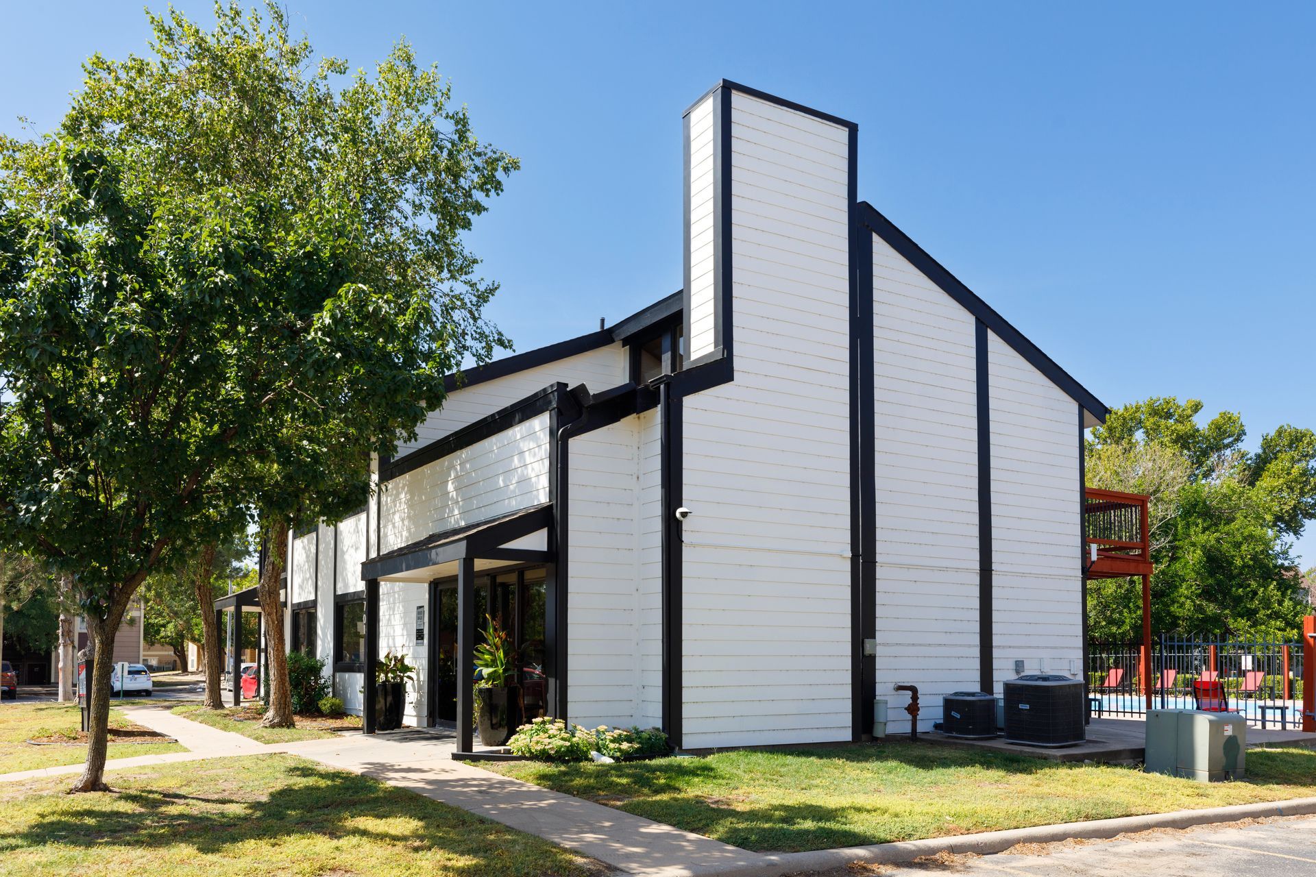 White and black multi-unit building under a blue sky with trees and a playground.