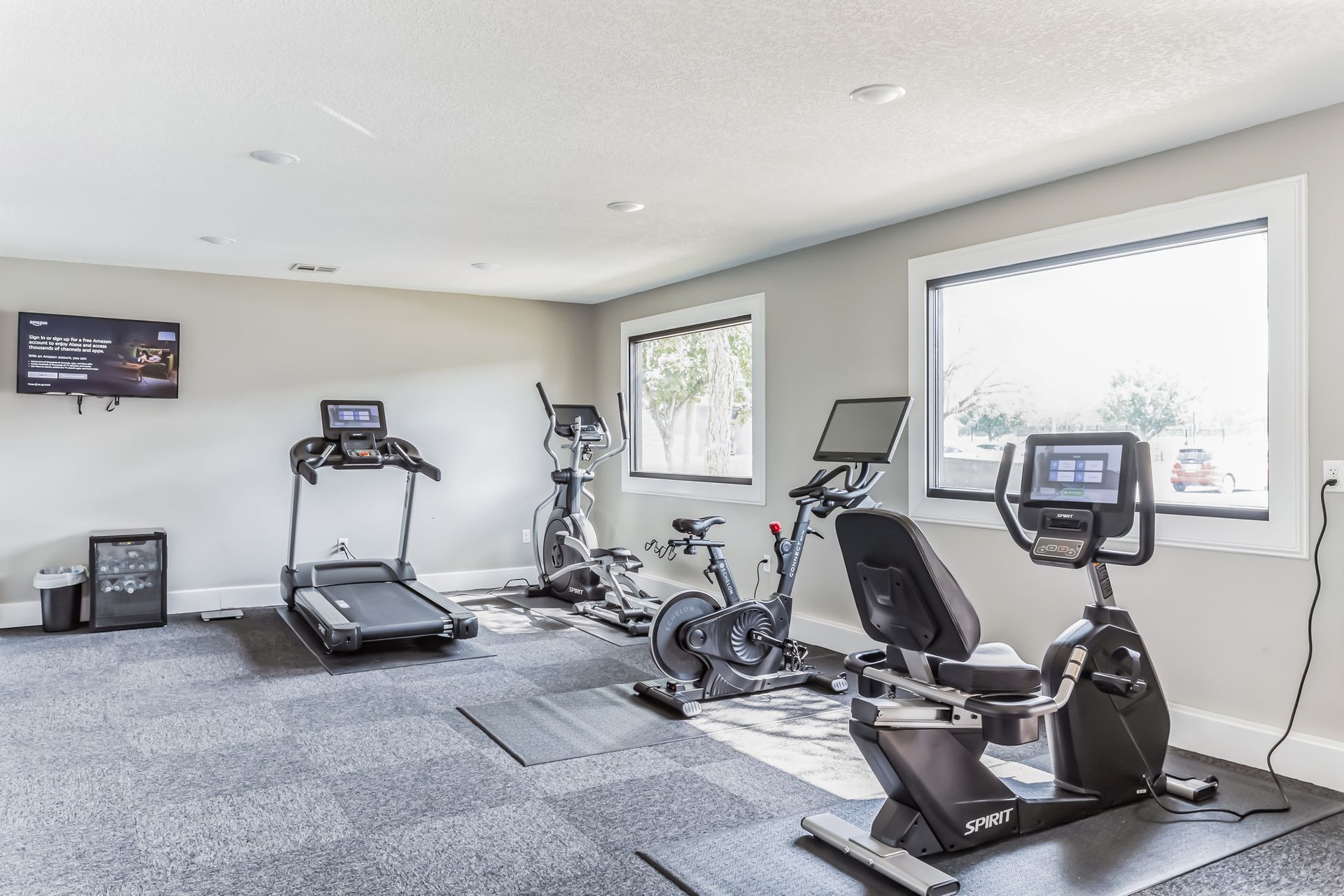 Gym with exercise equipment, including a treadmill, elliptical, and stationary bikes. Gray walls and carpet.