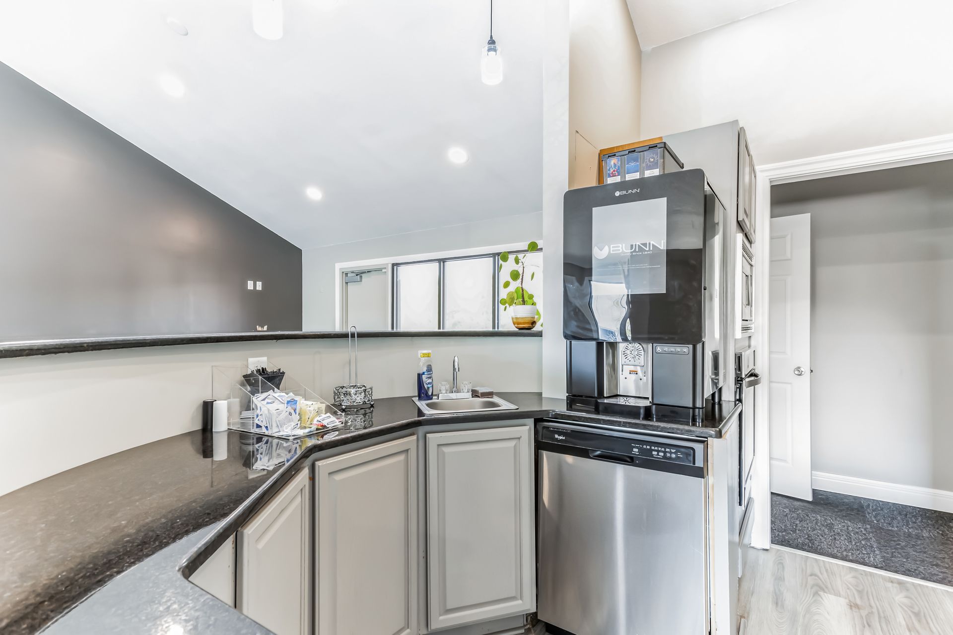 Kitchen with black countertops, stainless steel appliances, and a coffee machine. A doorway is visible.