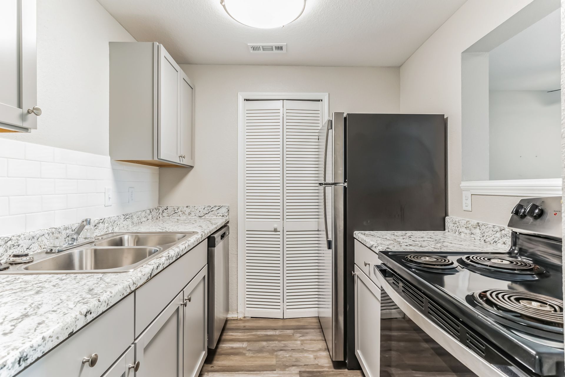 Kitchen with gray cabinets, granite countertops, stainless steel appliances, and white brick backsplash.