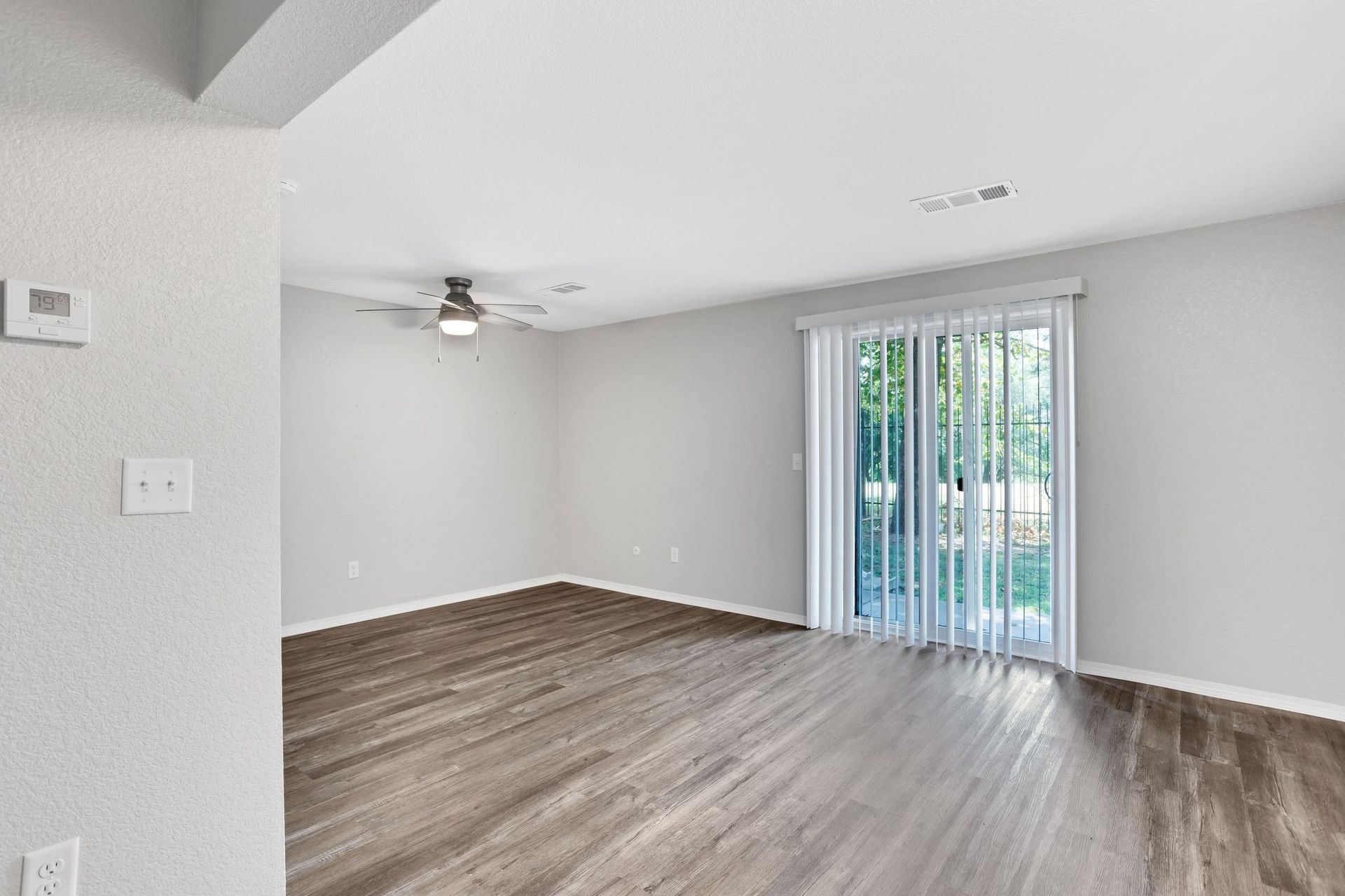Empty living room with gray walls, wooden floor, and sliding glass door to the outside.