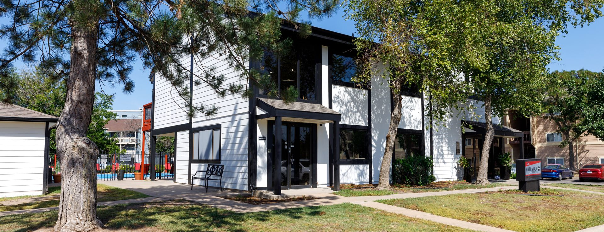 White and black building with two stories and large windows, trees, and a grassy yard.