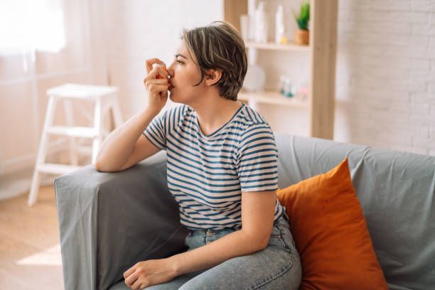 A Woman Is Sitting On A Couch Taking Medication For Her Asthma — Chicago, IL — Chicagoland Home Physicians