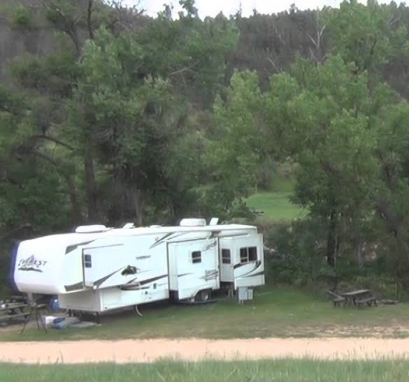 A white rv parked in a grassy field with trees in the background