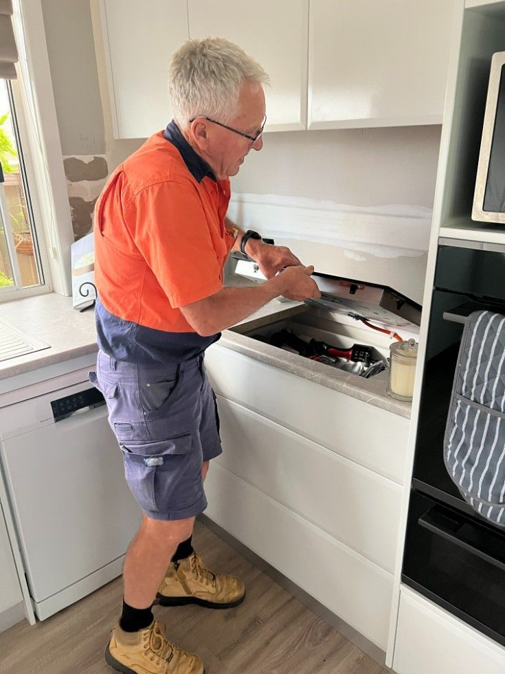 A Man is Working on a Stove in a Kitchen — Rob Fritsch Electrical in Wagga Wagga, NSW