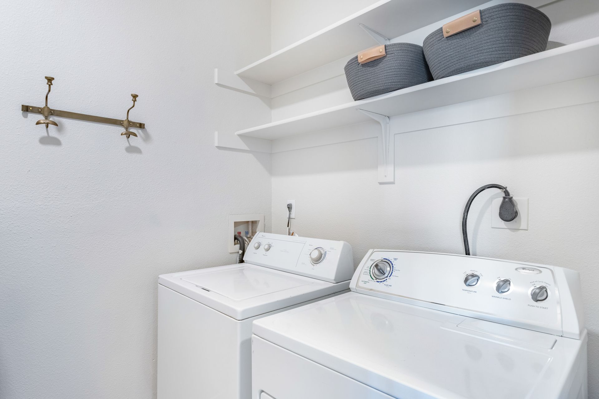 Laundry room with white washer and dryer, shelves with baskets, and wall hooks.