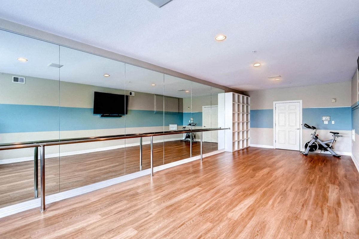 Dance studio with mirrored wall, ballet bar, wooden floor, blue and white walls, and exercise bike.