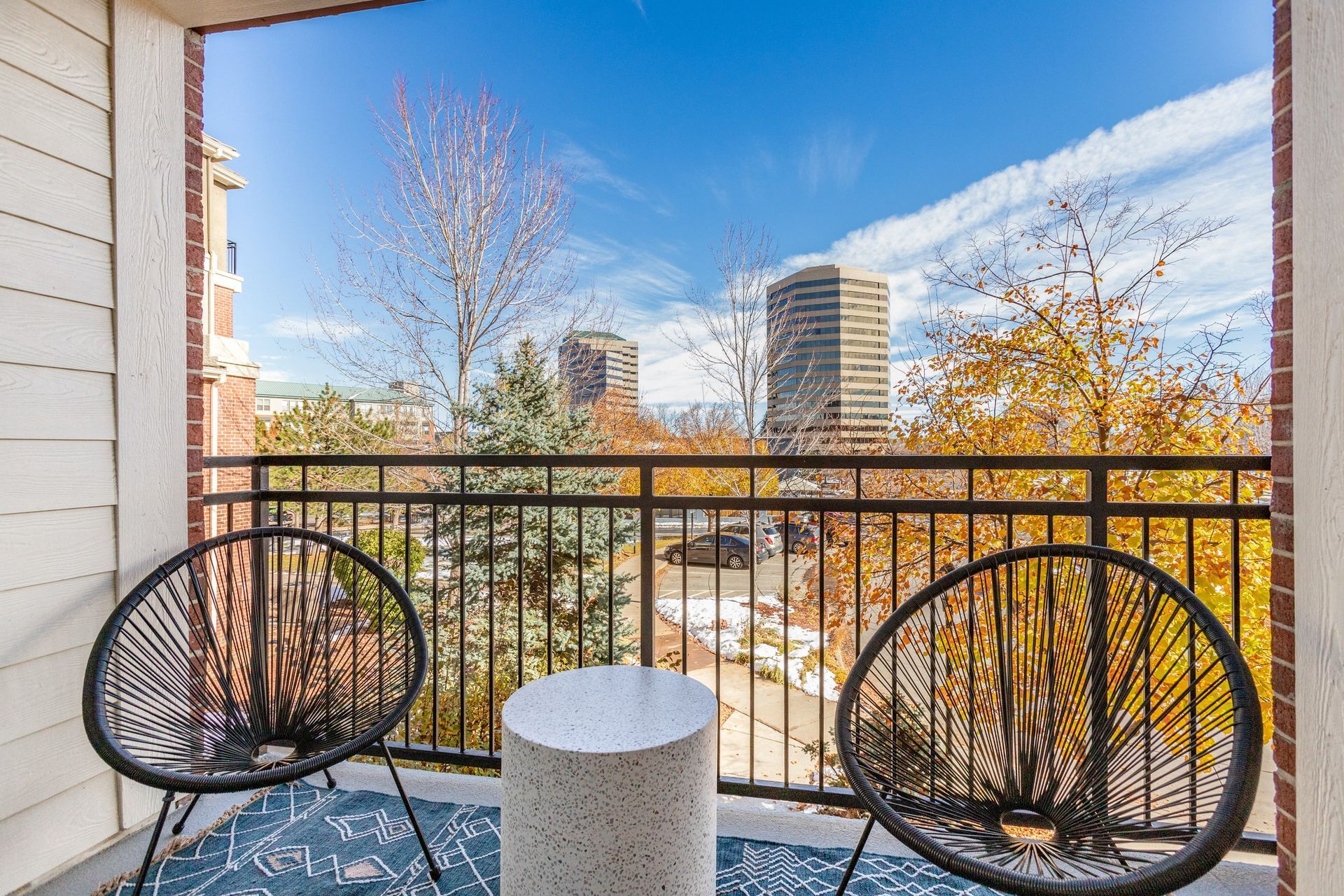Balcony with two black chairs, a small table, and a city view on a sunny day.