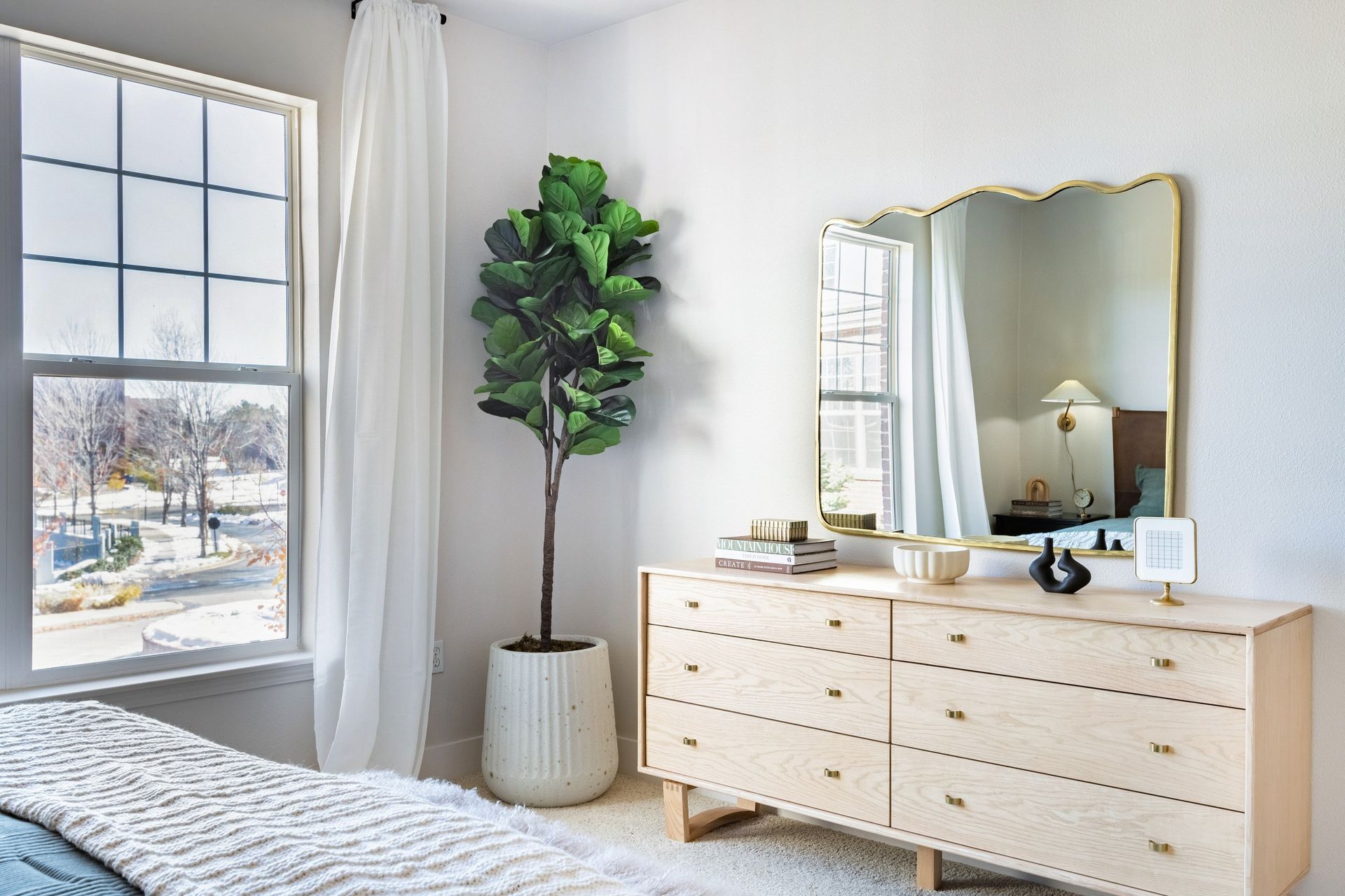 Bedroom with dresser, large window, and a potted fiddle-leaf fig tree. Natural light fills the room.